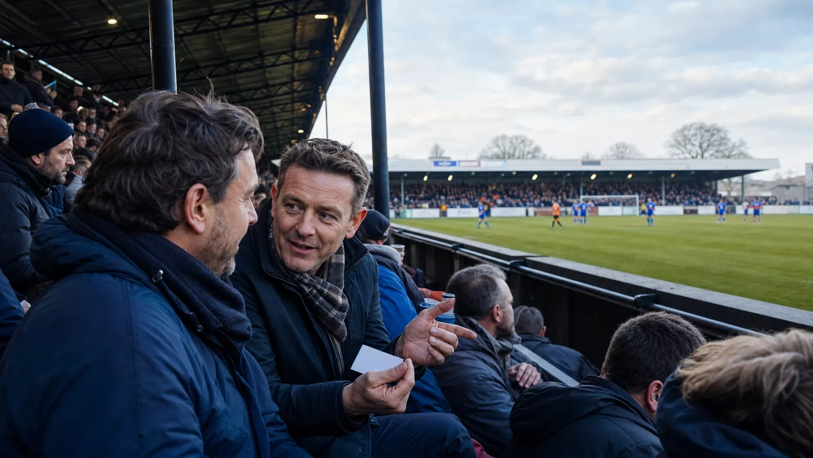 Two supporters discussing a business opportunity in a packed non-league football stand